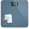 A blue bathroom scale with a digital LCD screen displaying weight, showing a card that reads 'AccuCheck' and a set of batteries in front of the scale.