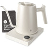 An electric gooseneck kettle with a matte white finish, placed on a black base, featuring a booklet that reads 