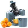A blue cold press juicer with oranges and a juice cup in the foreground.
