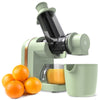 A green cold press juicer with oranges and a juice cup in the foreground.
