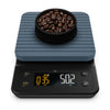 A digital kitchen scale with a blue cover and black matte finish, featuring a digital display showing weight and timer, with a bowl of coffee beans on top.
