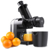 A black cold press juicer with oranges and a juice cup in the foreground.