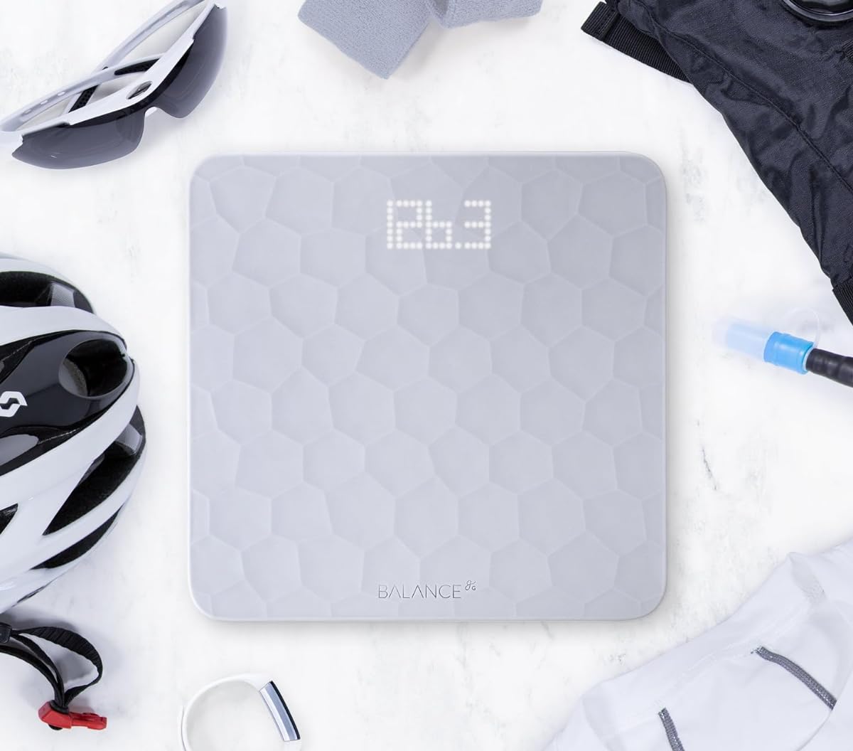 Gray digital scale with geometric pattern on a white surface, surrounded by gym equipment.