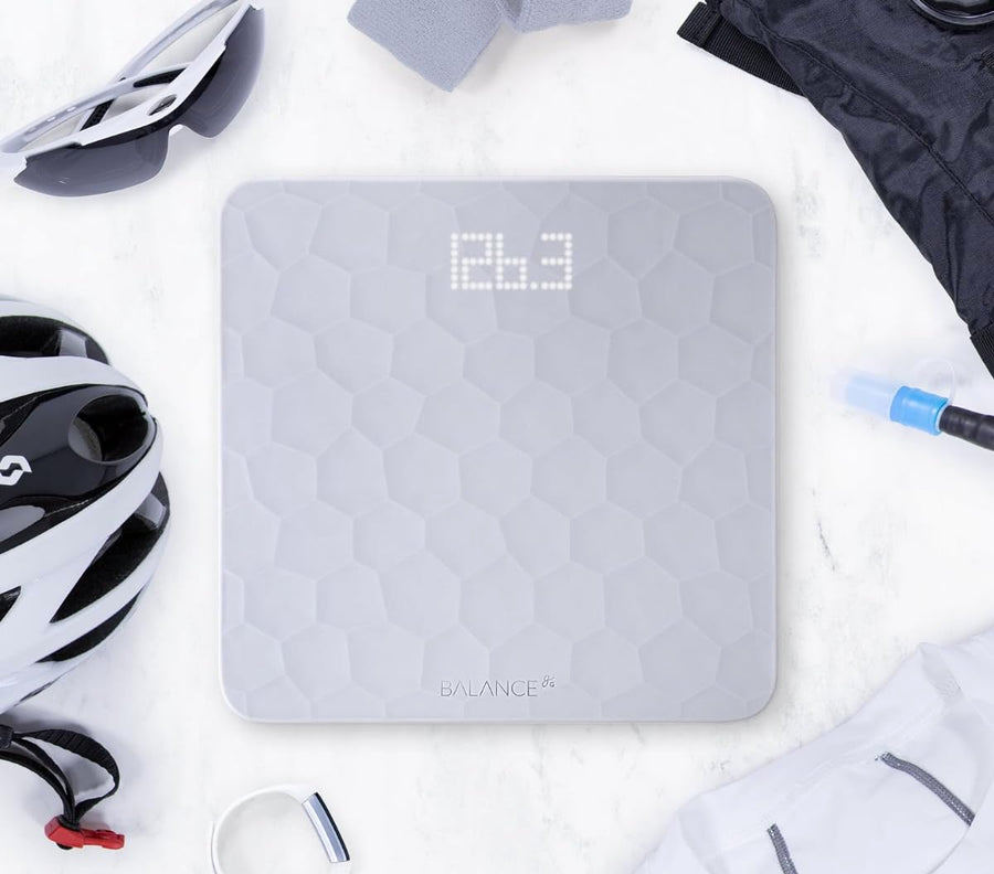 Gray digital scale with geometric pattern on a white surface, surrounded by gym equipment.