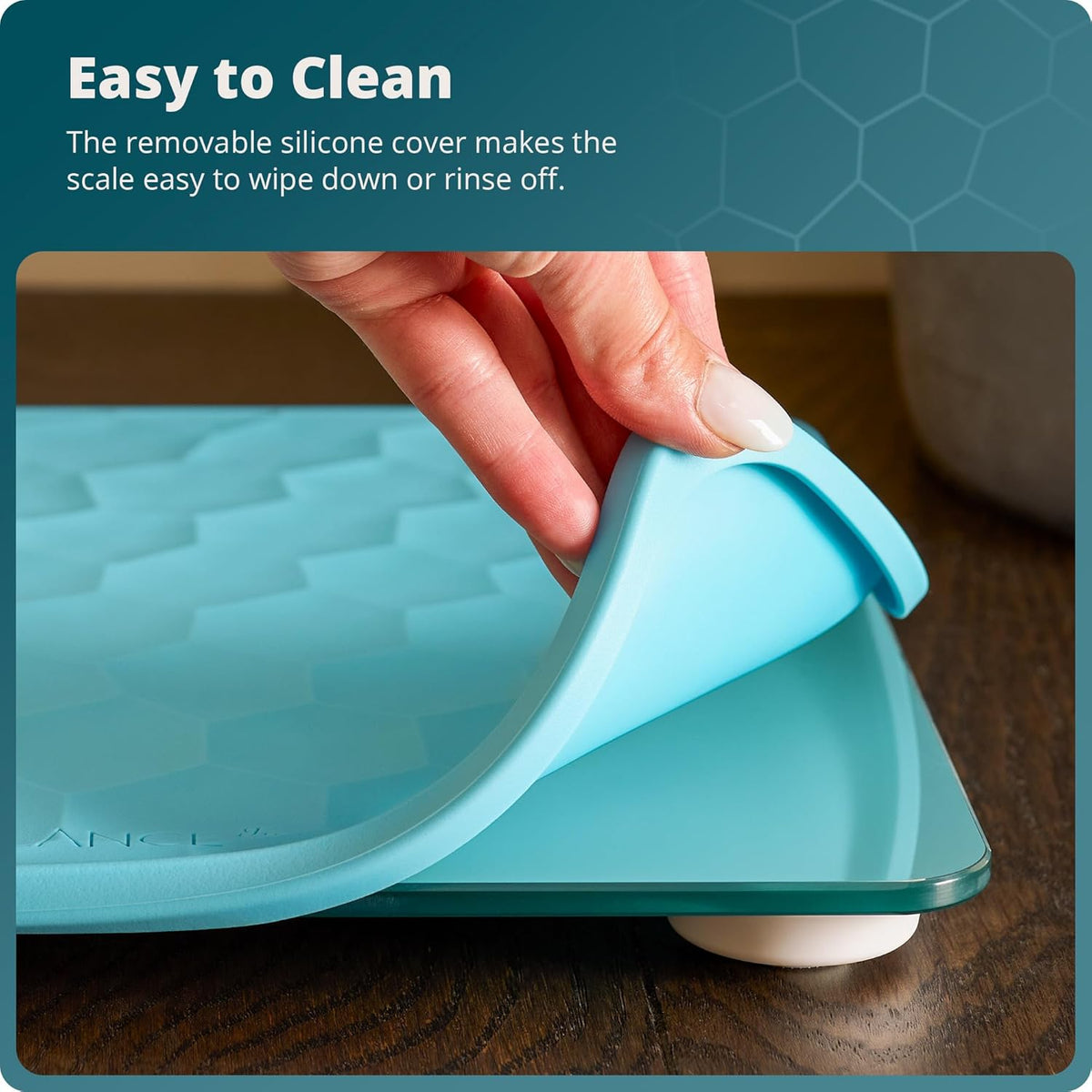 Blue scale with a removable silicone cover being held by a hand on a wooden surface. Text reads, "Easy to Clean: The removable silicone cover makes the scale easy to wipe down or rinse off."