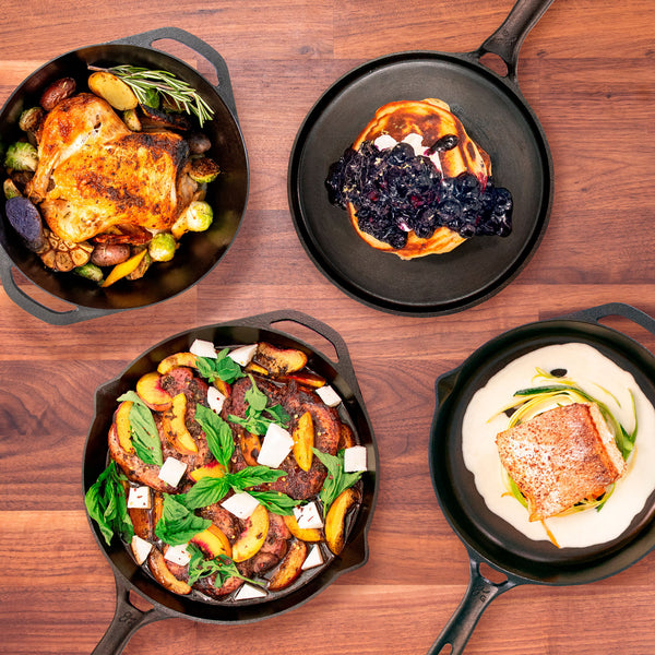 A cast iron dutch oven with roasted chicken, griddle with blueberry pancakes, 12 inch skillet with grilled peaches, and 10 in skillet with salmon. 